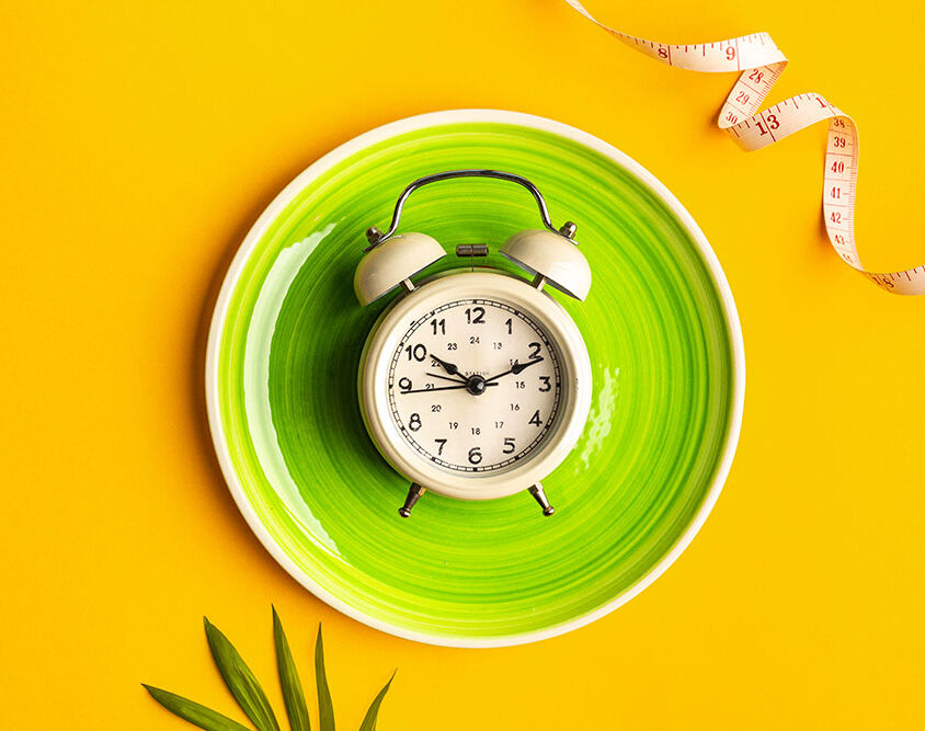 Composition with plate, alarm clock and measuring tape on a colored background Diet concept and weight loss plan